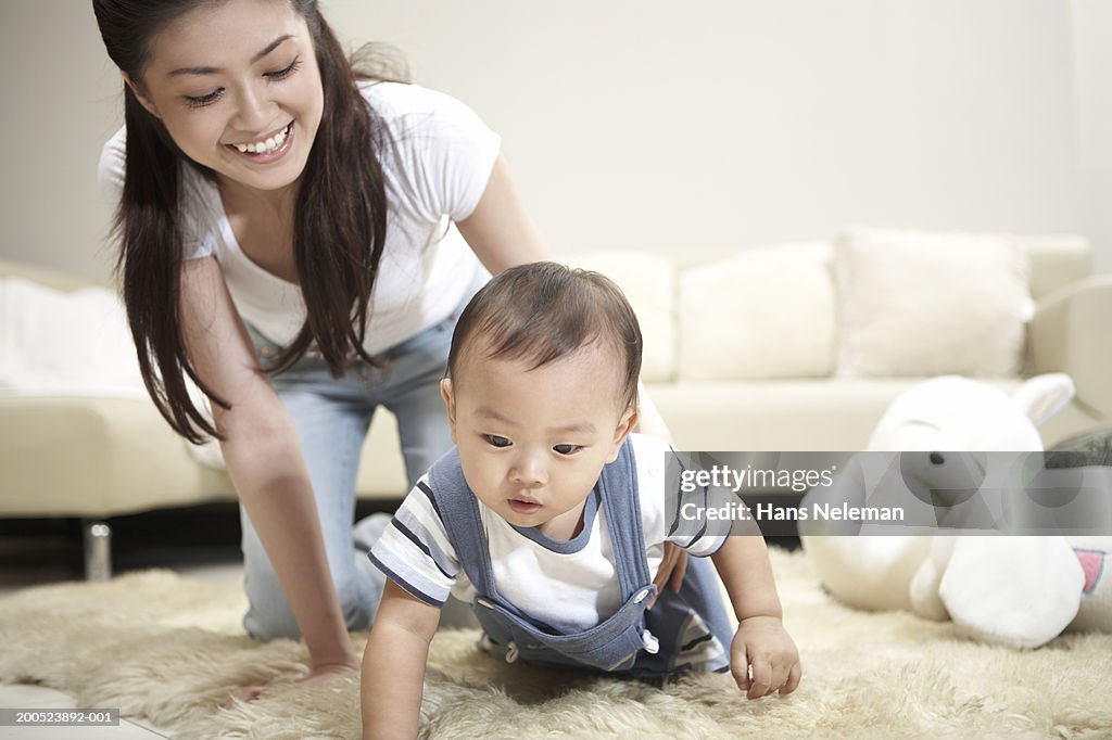 Young mother watching baby boy (9-12 months) crawling in living room