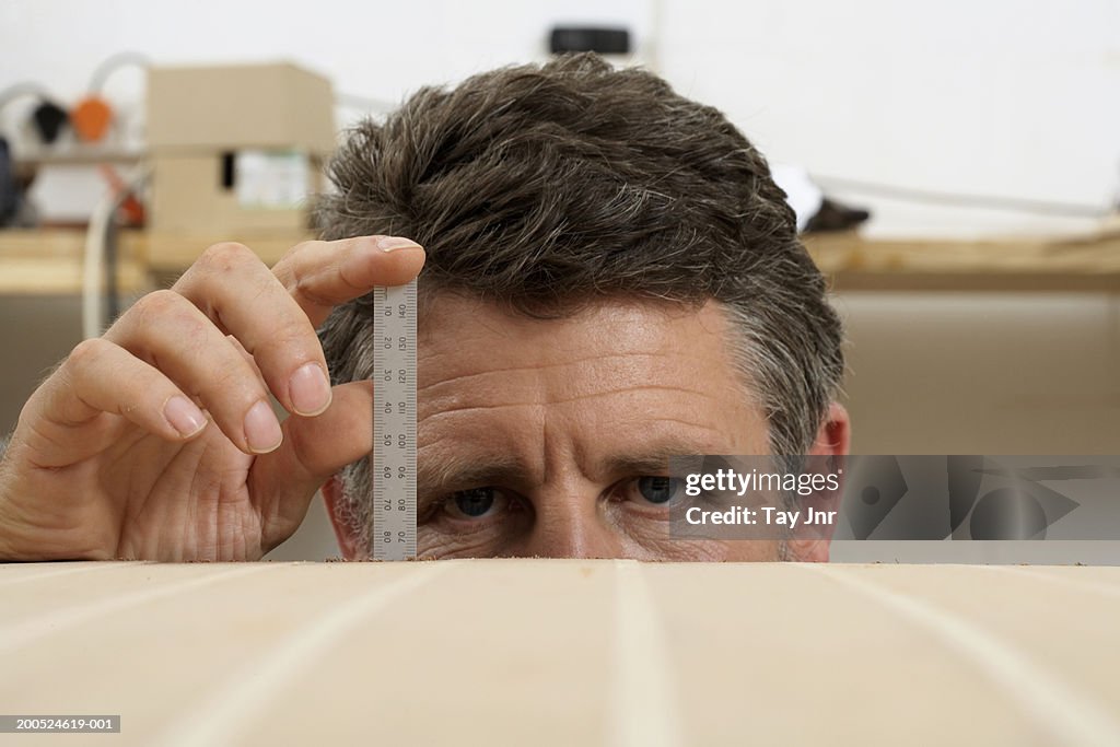 Mature man measuring boat with ruler, close-up, high section