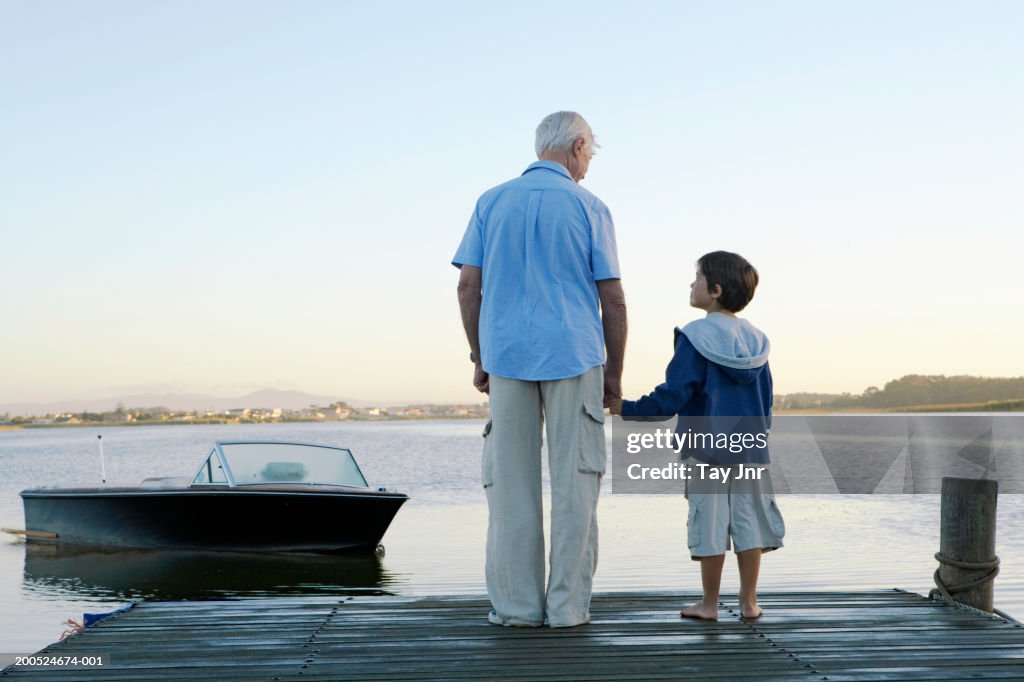 Grandfather and grandson (6-8) holding hands on jetty, rear view