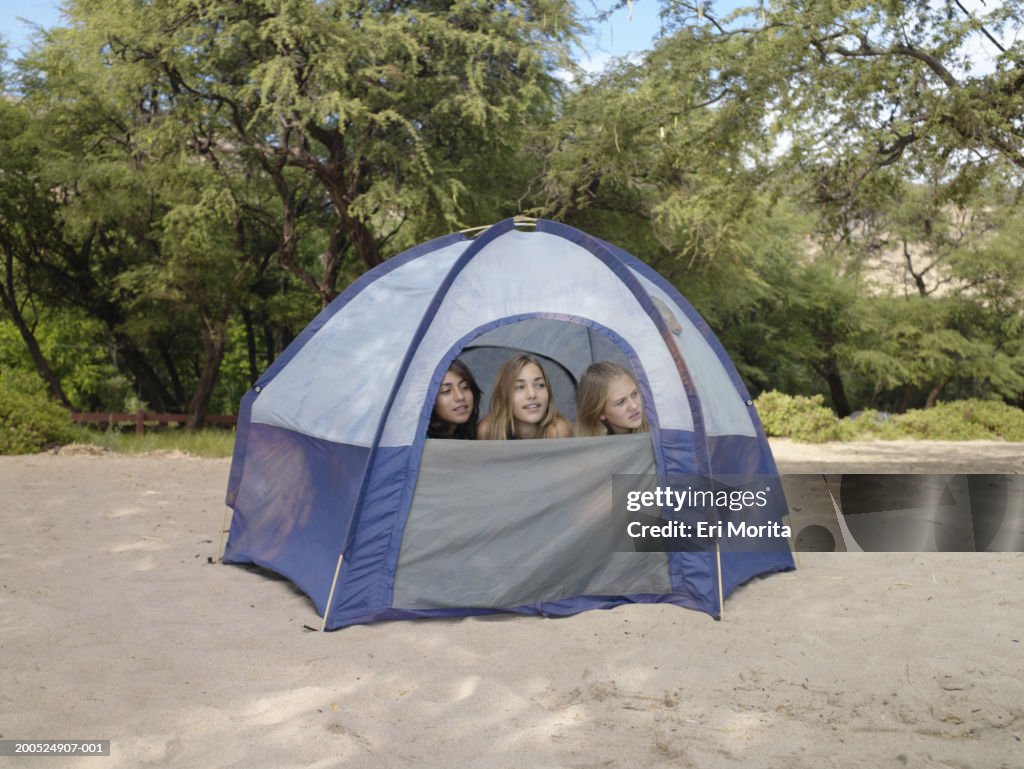 Three teenage girls (12-14) looking out tent opening at beach