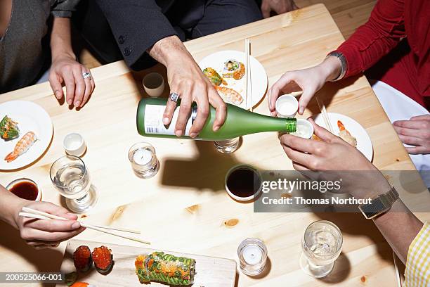 four adults eating sushi and drinking sake, mid section, elevated view - saké bildbanksfoton och bilder