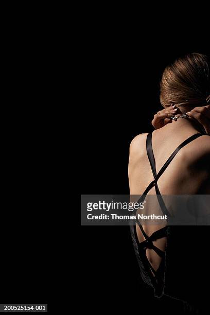 young woman in evening gown clasping necklace, rear view - vestito da sera femminile foto e immagini stock