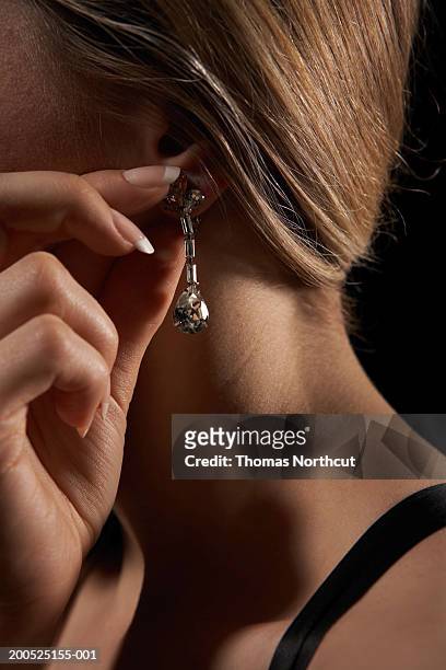 young woman adjusting earring, side view - ohrring stock-fotos und bilder