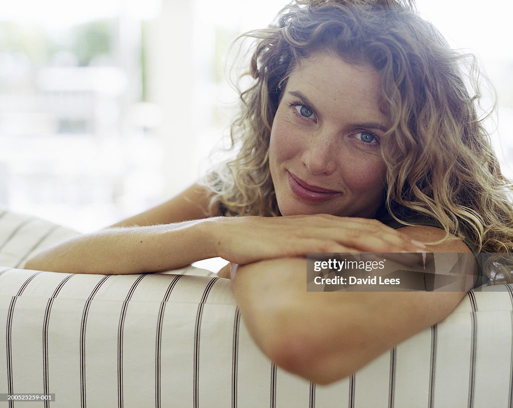 Woman leaning on sofa, smiling, portrait