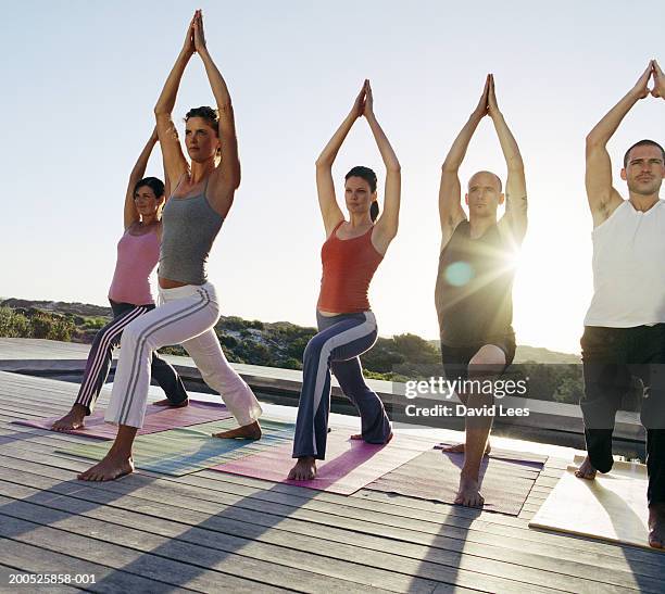 men and women performing yoga poses on decking by pool at sunset - sun deck stock pictures, royalty-free photos & images