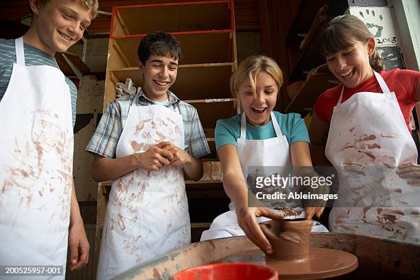 girl (13-15) potting on wheel surrounded by classmates, smiling - potters wheel stock pictures, royalty-free photos & images