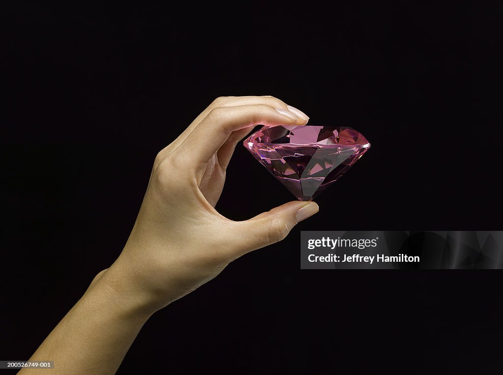 Woman holding large pink diamond against black background