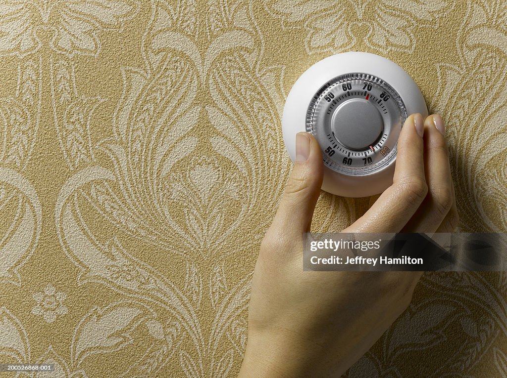 Woman adjusting thermostat on beige wallpapered wall, close-up