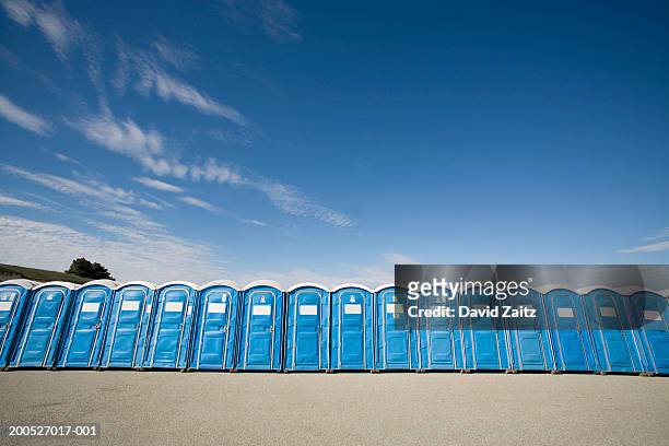 row of blue plastic portable toilets against blue sky, low angle view - mietklo stock-fotos und bilder