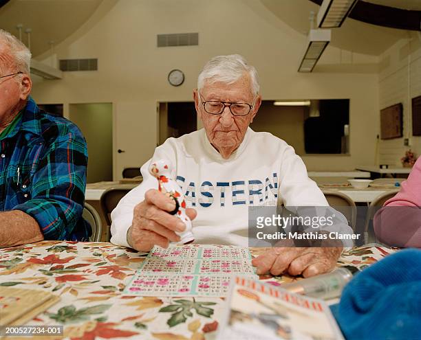 senior man playing bingo, sitting by table - bingo fotografías e imágenes de stock