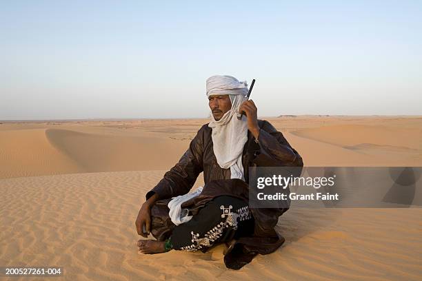 niger, south sahara desert, tuareg man sitting cross-legged, using satellite phone, in desert - touareg 個照片及圖片檔