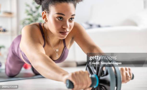 a good-looking  young multiracial girlexercises at home and strengthens her stomach with ab roller sports equipment. - black female bodybuilder stock pictures, royalty-free photos & images