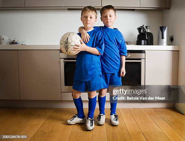 boys (8-10) in football strip standing in kitchen, portrait - twins boys stock-fotos und bilder