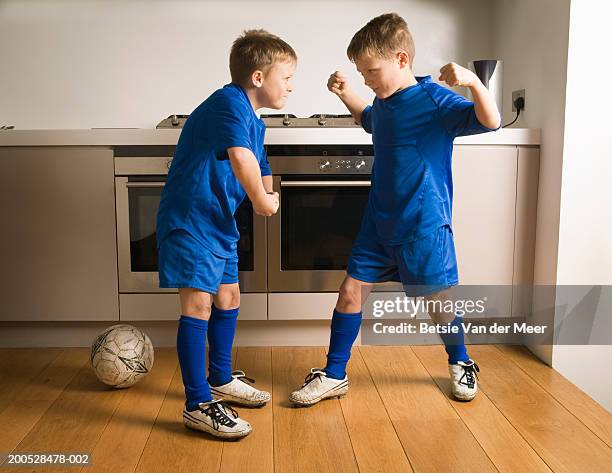 boys (8-10) in football strip flexing muscles in kitchen - sibling rivalry stock pictures, royalty-free photos & images