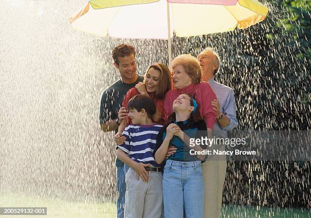 three-generational family standing under sun umbrella in rain, smiling - mother protecting from rain stockfoto's en -beelden