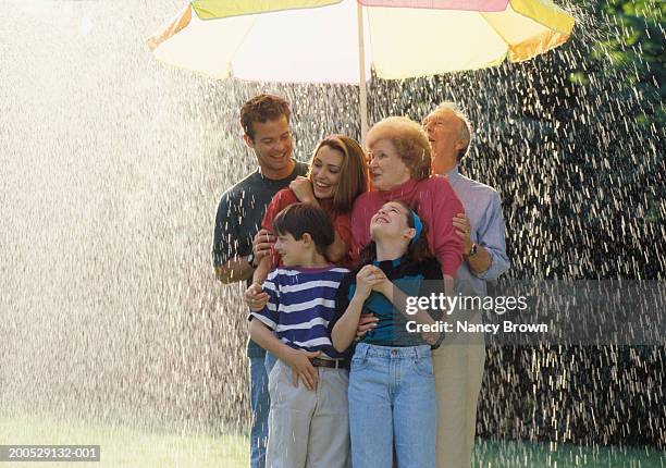 three-generational family standing under sun umbrella in rain, smiling - mother protecting from rain stock pictures, royalty-free photos & images