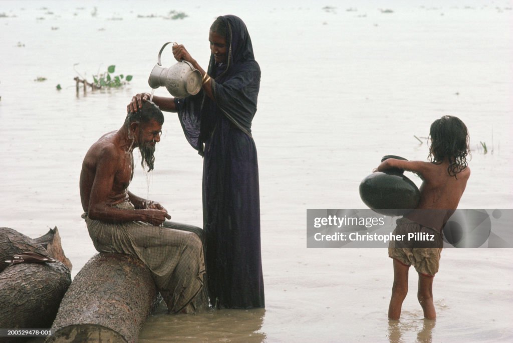 India, Bangladesh, woman standing in river washing man's hair...