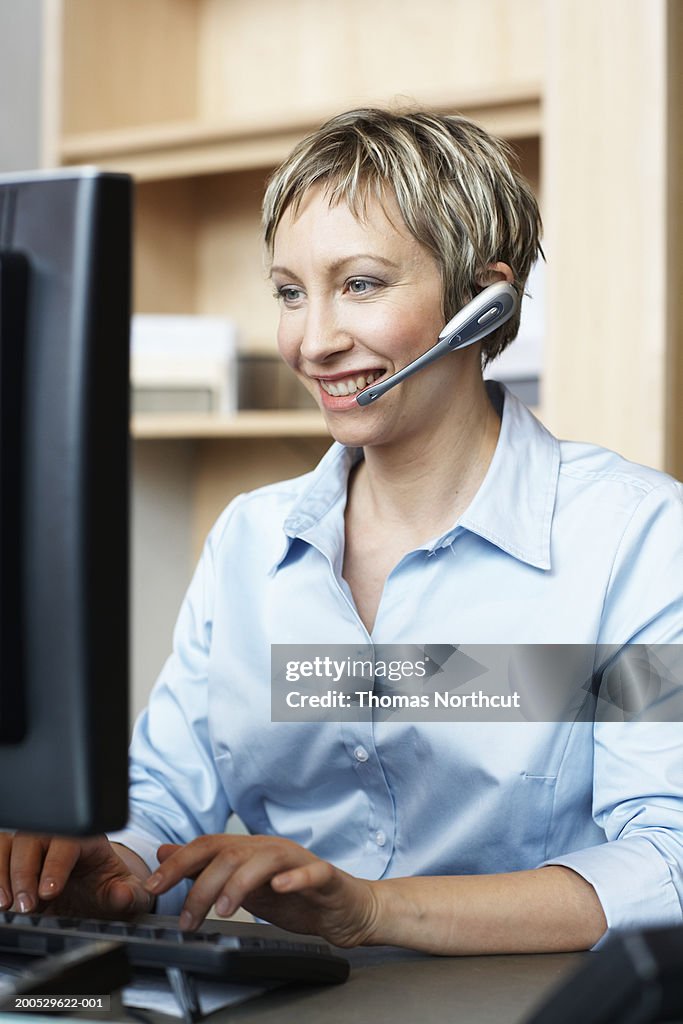 Businesswoman wearing headset and using computer, smiling