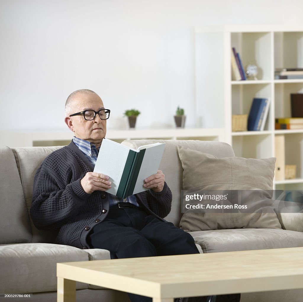 Senior man reading book on sofa