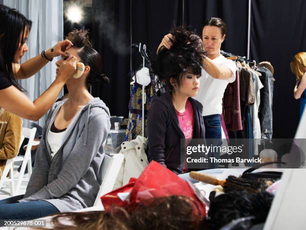 two models having hair styled and make-up applied by stylists - backstage hairdresser stock-fotos und bilder