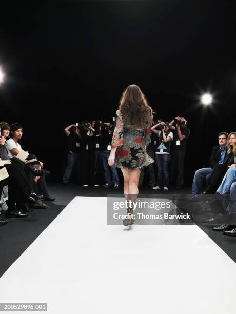 young female model on catwalk, group of photographers in background - podium de défilé photos et images de collection