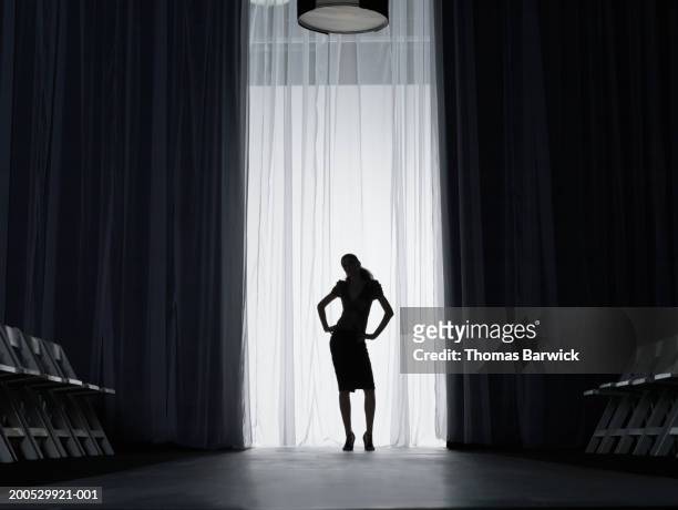 silhouette of young woman standing on catwalk, hands on hips - fashion show fotografías e imágenes de stock