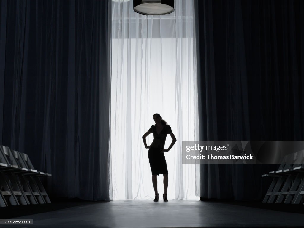Silhouette of young woman standing on catwalk, hands on hips