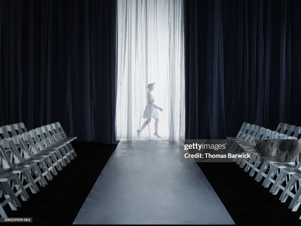 Female model (15-17) walking backstage at fashion show, side view