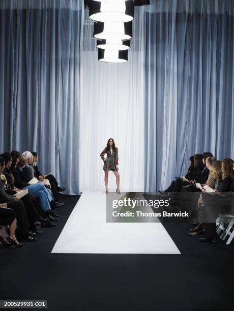 spectators watching young female model standing on catwalk - fashion show foto e immagini stock