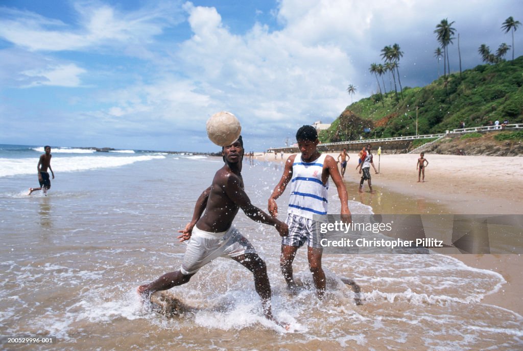 Brazil, Salvador City, men playing football in surf on beach...