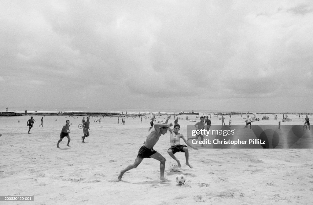 Brazil, boys playing football in surf on beach (B&W)