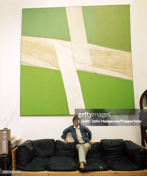 English artist and painter Sandra Blow posed on a large sofa in a studio workplace in England circa 1970. Hanging on the wall behind the artist is...