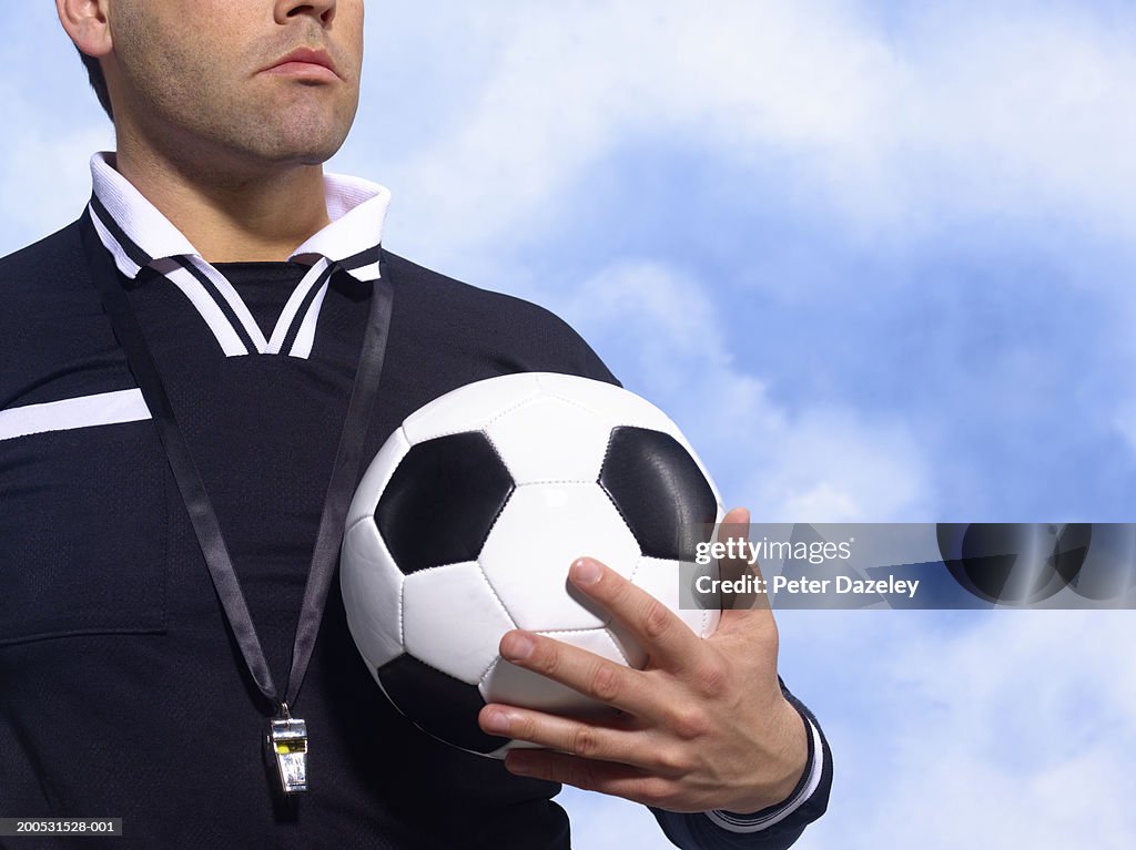 Referee holding football, with whistle around neck, mid section