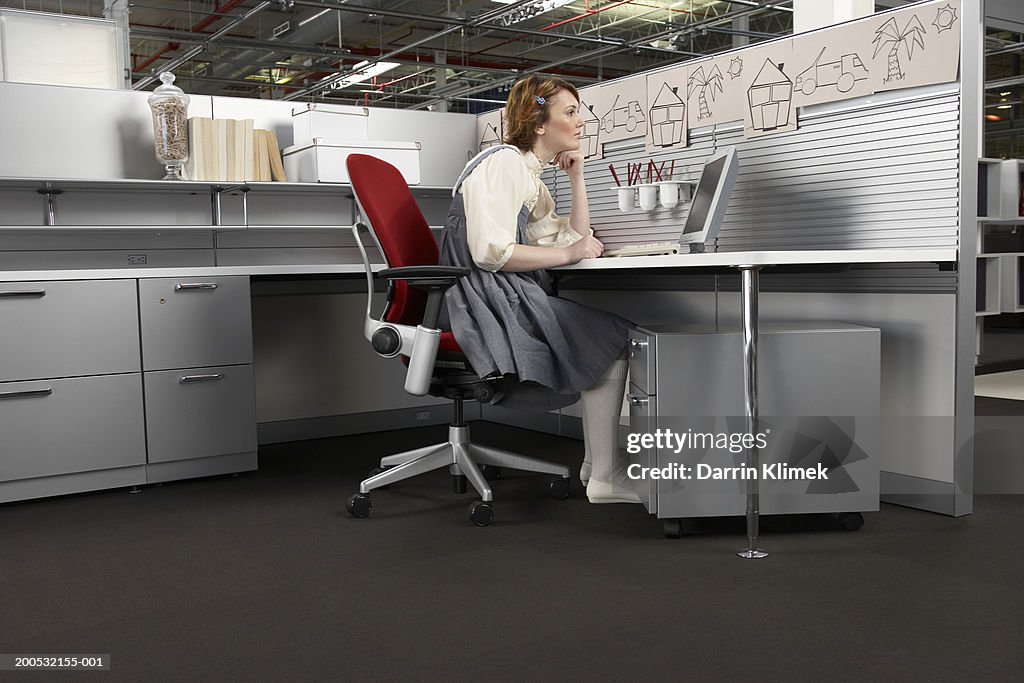 Woman at desk looking at child's drawings on cubicle partition