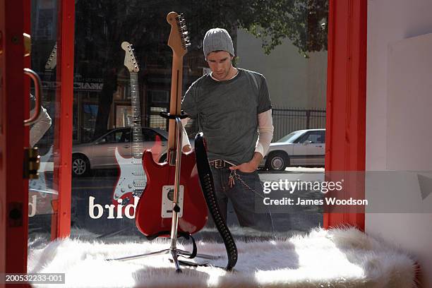 young man looking at guitar in shop window, view through glass - guitar shop stock pictures, royalty-free photos & images