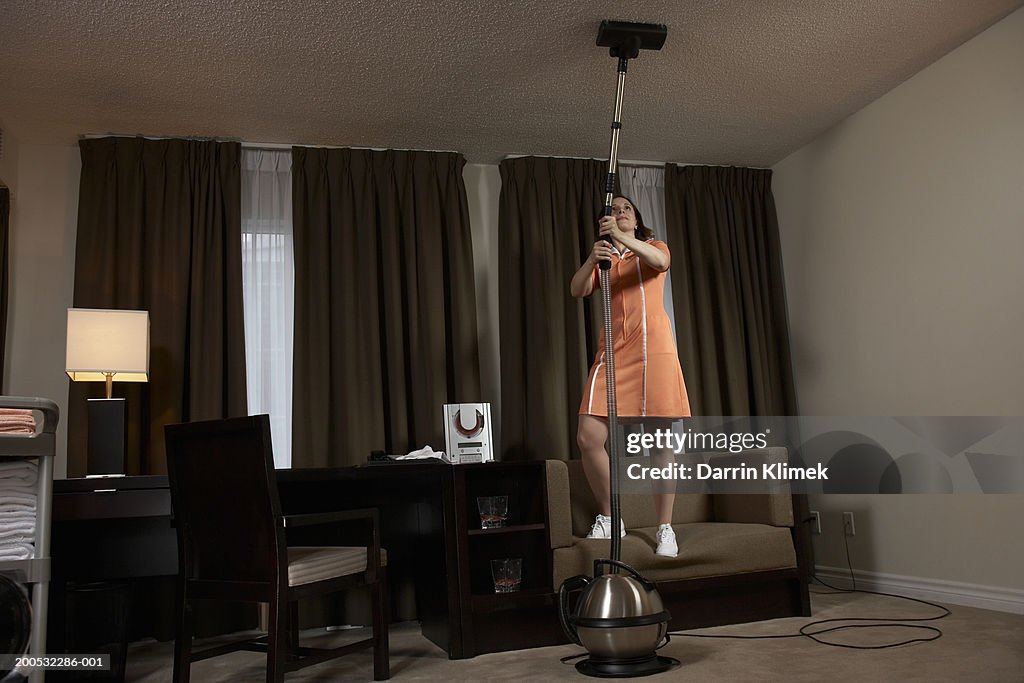 Chambermaid vacuuming hotel room ceiling