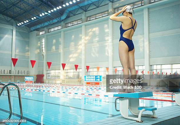 young female swimmer adjusting swimming cap atop starting block - schwimmer startblock stock-fotos und bilder