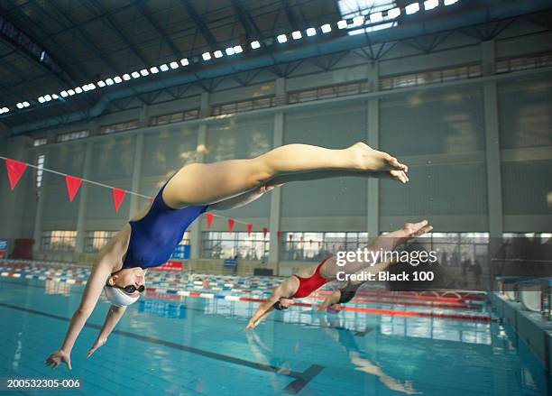 young female swimmers diving into swimming pool, side view - dive stockfoto's en -beelden