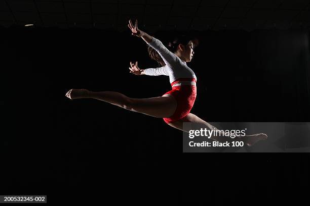 young female gymnast leaping in midair, arms outstretched, side view - turnen stock-fotos und bilder