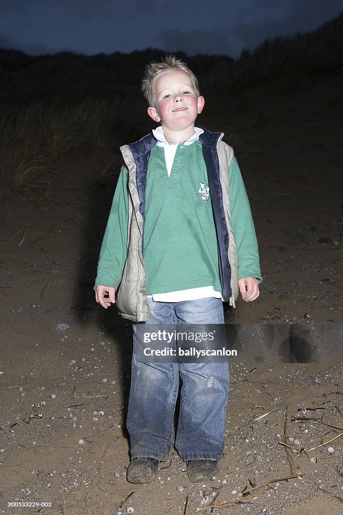 Boy (5-6) standing on beach, smiling, portrait