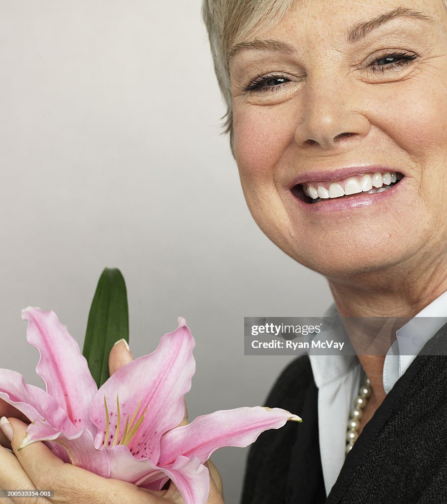 Mature woman holding flower, smiling, portrait