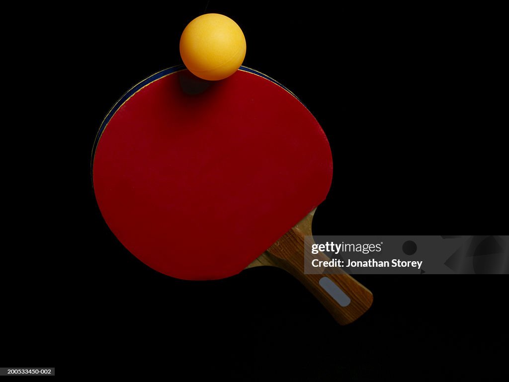 Ball balancing on table tennis bat, close-up, against black background