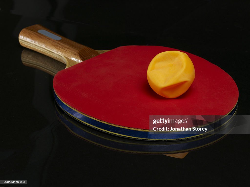 Broken ball on table tennis bat, close-up, against black background