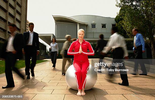 young woman sitting in yoga pose on exercise ball in busy street - hands in her pants fotografías e imágenes de stock