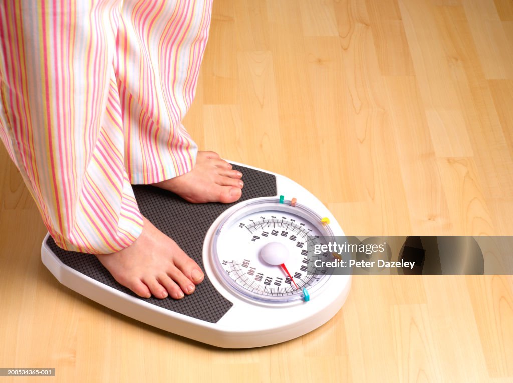 Woman standing on scales, wearing pyjamas, low section
