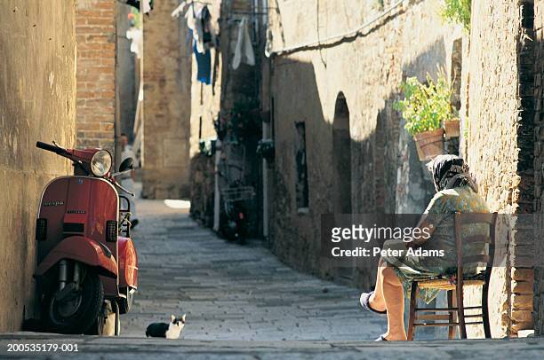 italy, tuscany, senior woman sitting in street by cat - old woman cat stock-fotos und bilder