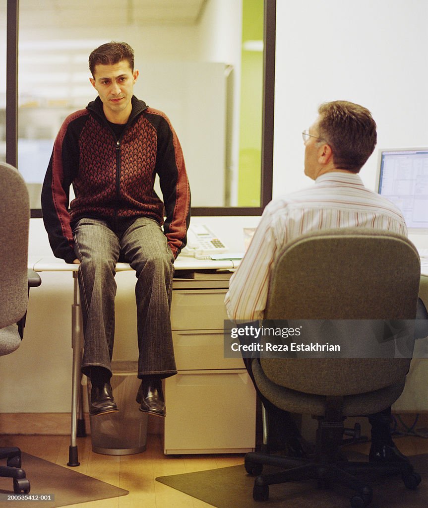 Businessman sitting on desk, talking to colleague