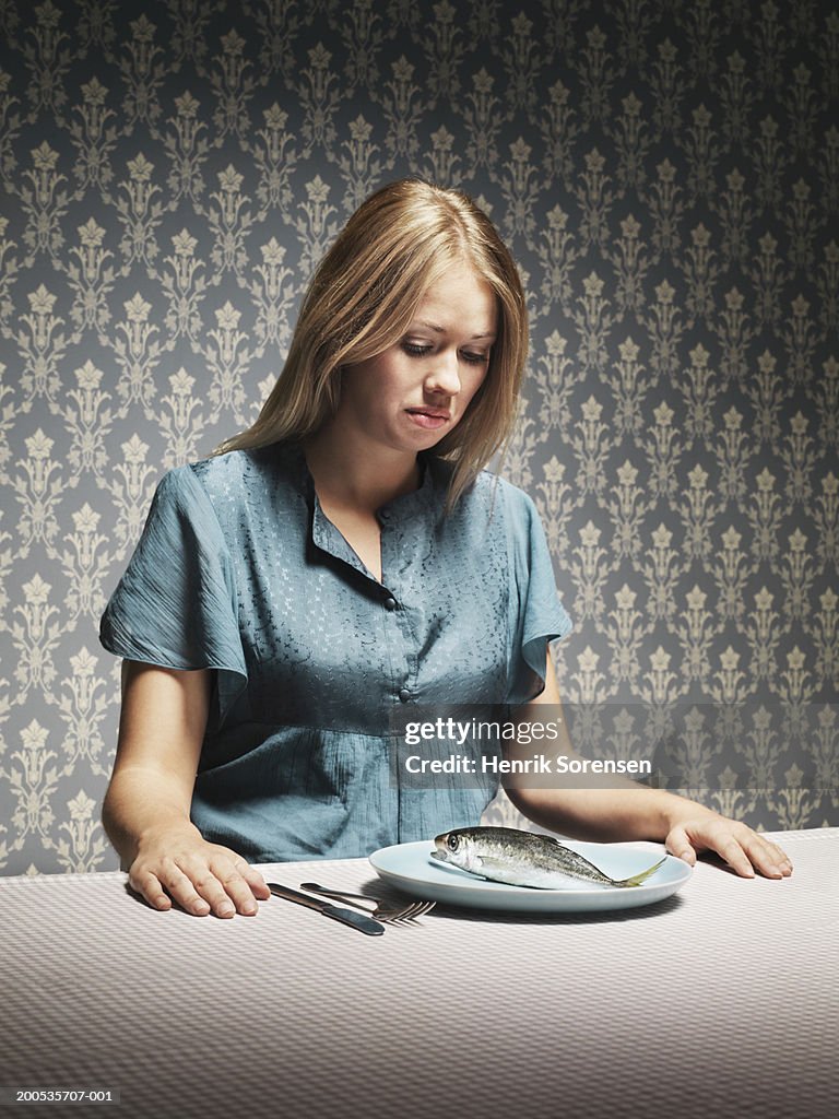 Woman looking at fish on plate at dinner table