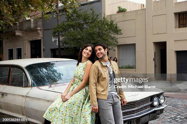 young couple sitting against car, smiling - two cars side by side stock pictures, royalty-free photos & images