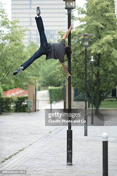 young man performing splits holding onto lamp post, rear view - street light post stock pictures, royalty-free photos & images